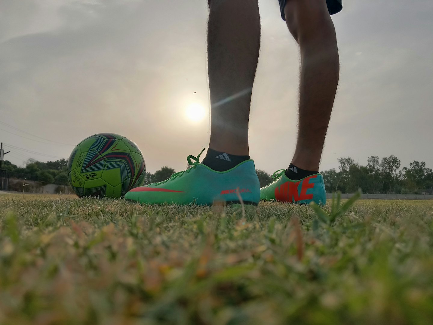 Persona de pie en un campo de hierba con un balón de fútbol cerca de sus pies.