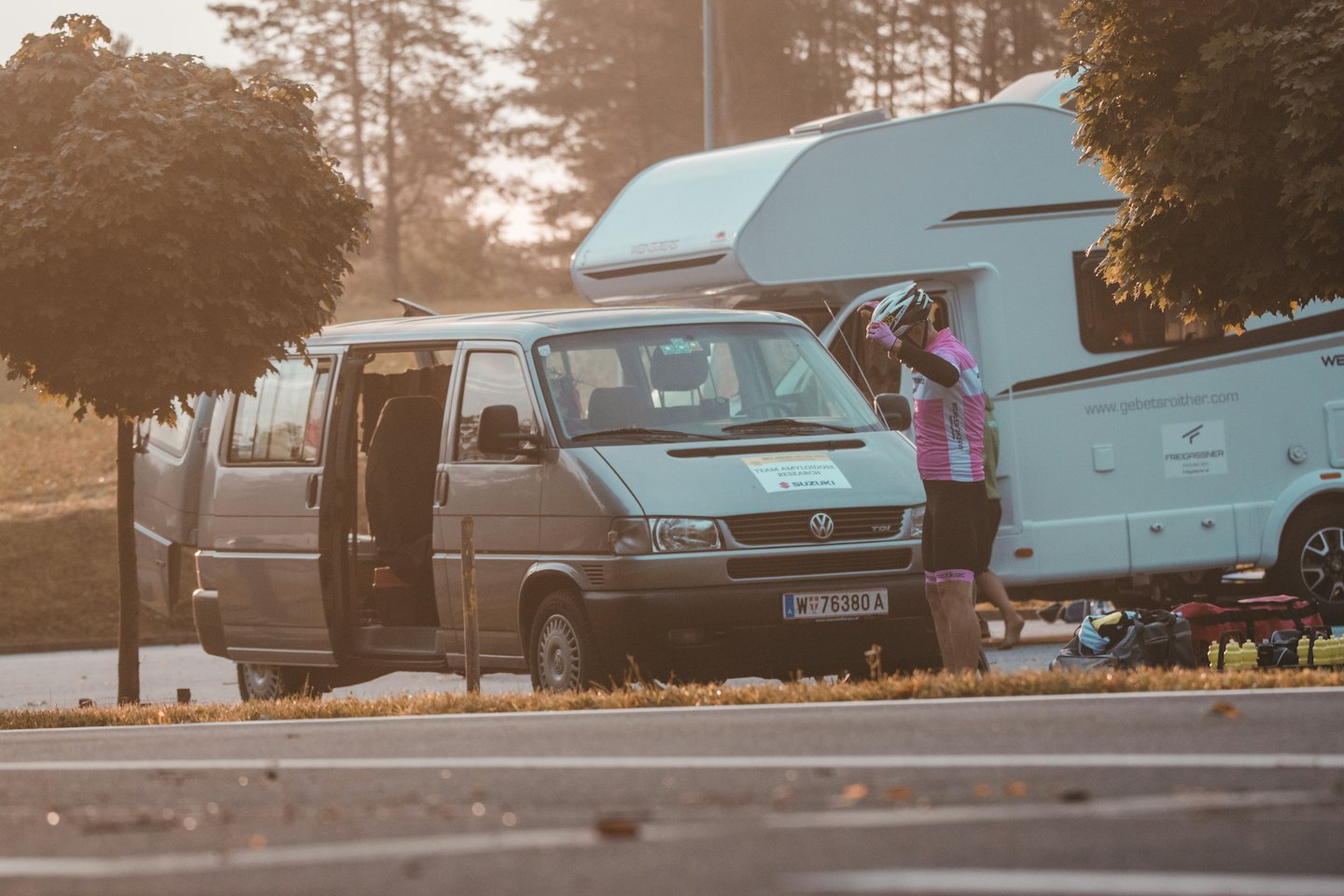 Ciclista se ajusta el casco junto a una furgoneta y una caravana para una actividad al aire libre.