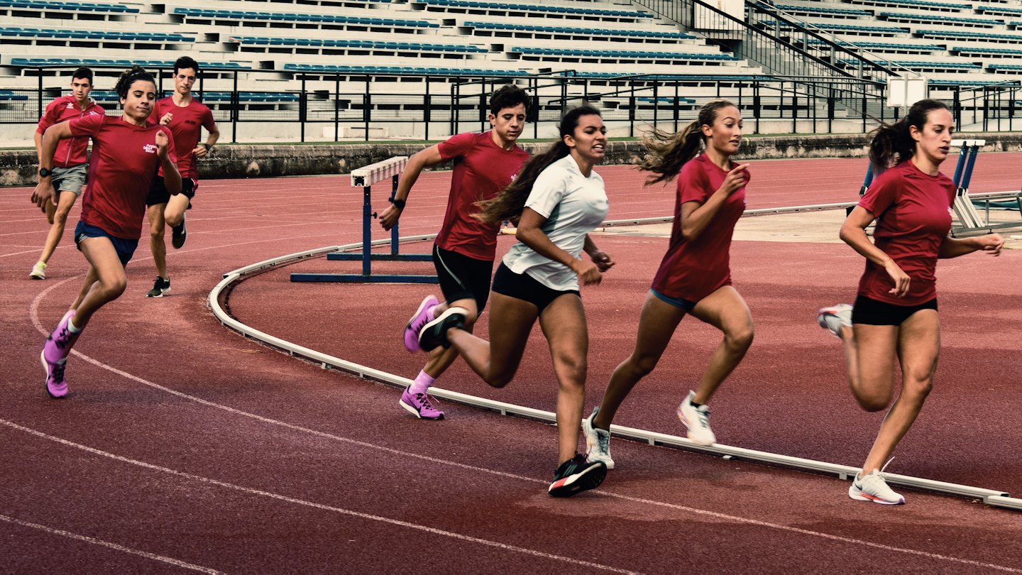 Siete atletas corren juntos en una pista roja en un estadio.